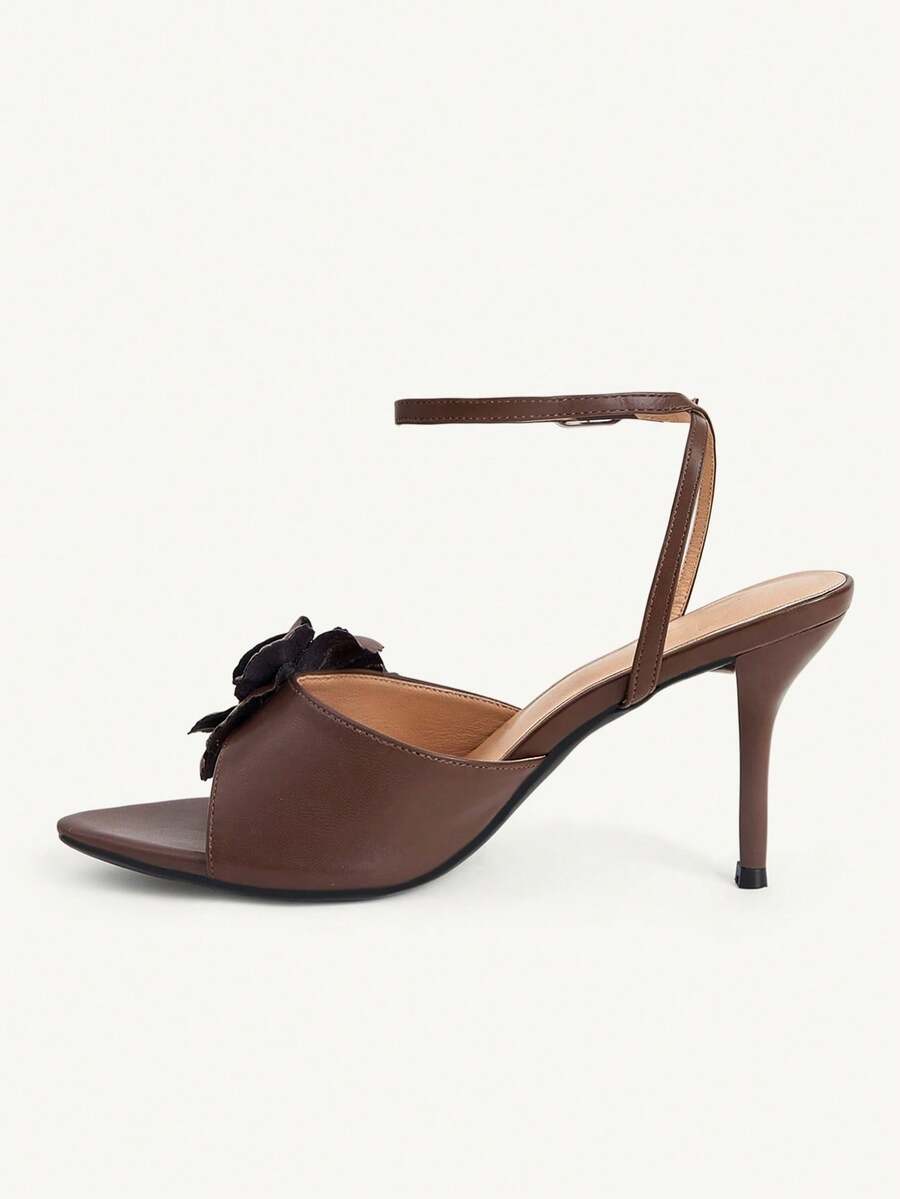 Champagne stiletto high heel sandals featuring a flower detail, open toe, and buckle back strap.