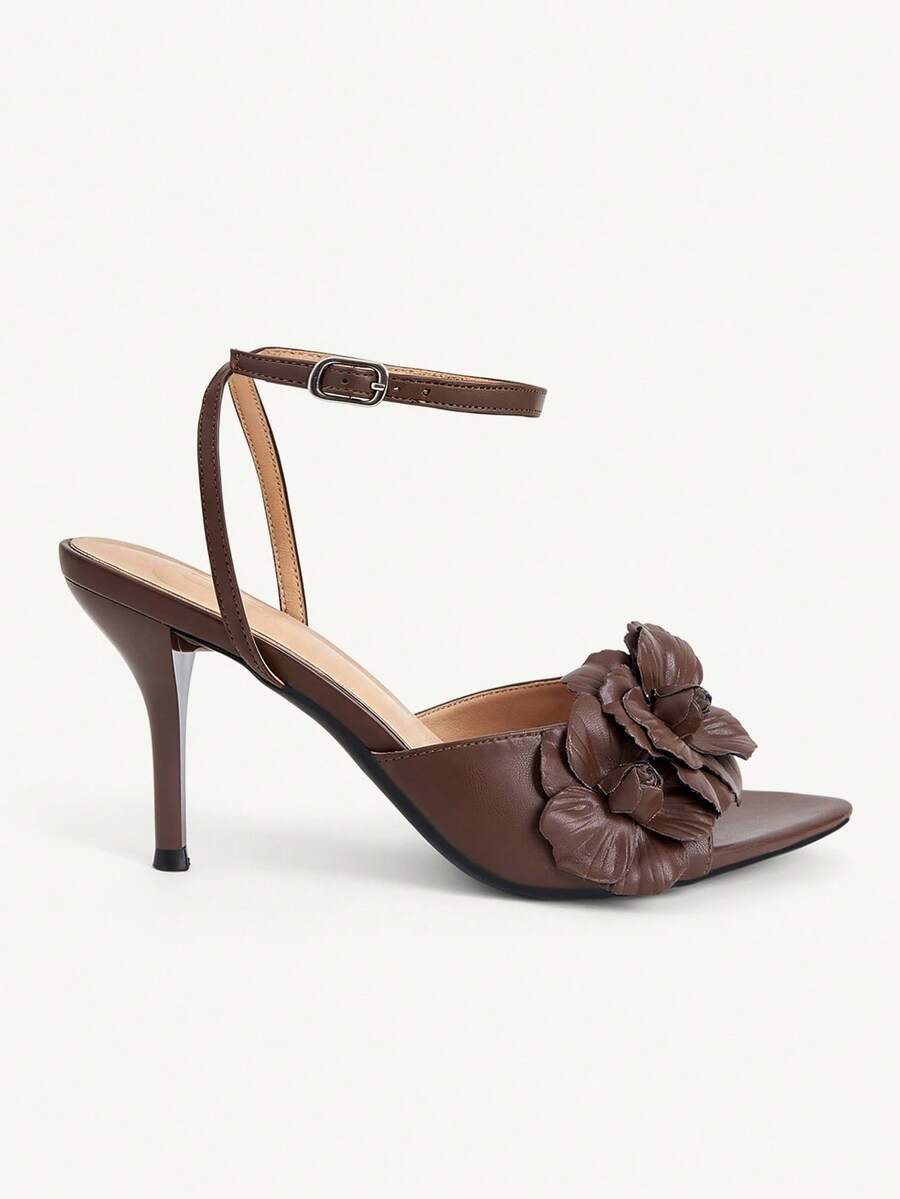 Champagne stiletto high heel sandals featuring a flower detail, open toe, and buckle back strap.