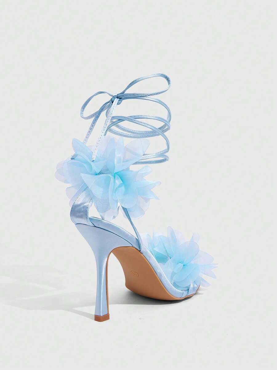 Women's open toe heeled sandals featuring 3D floral decor, satin lace-up ankle straps, and stiletto high heels.