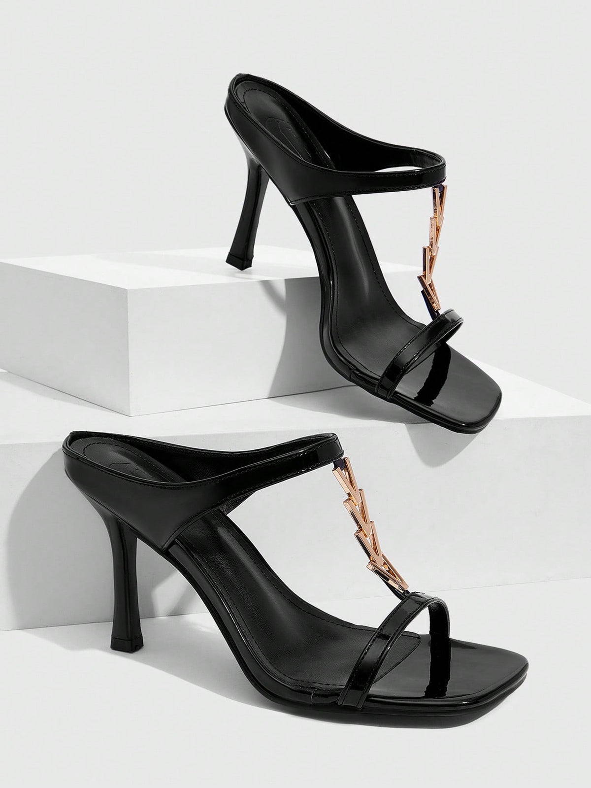 Women's black patent leather slip-on heeled sandals featuring a square toe, gold metal hardware, and sleek stiletto heels.
