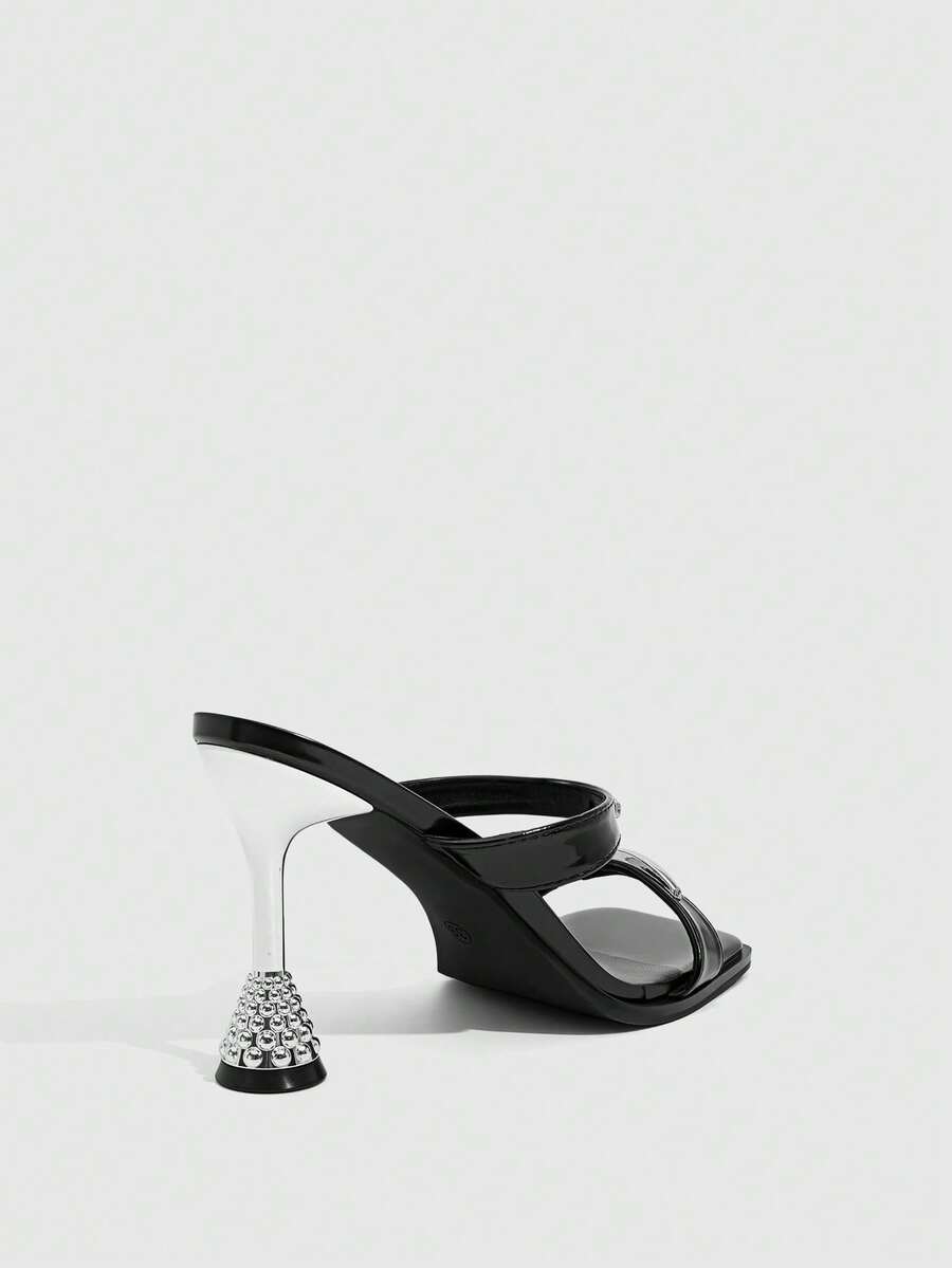 Women's black high-heeled sandals featuring an open square toe, stiletto heel, and decorative metal buckle strap detail.