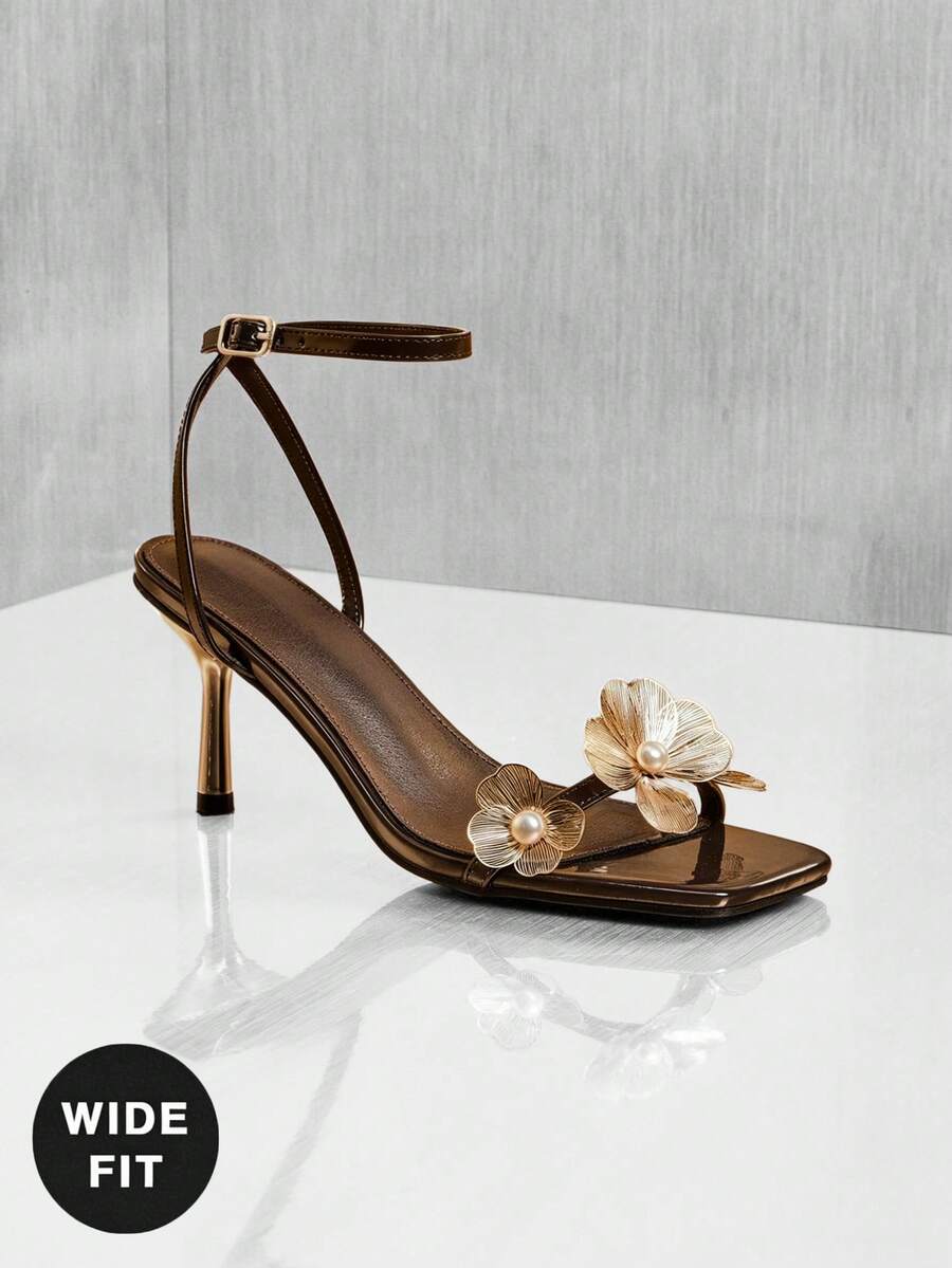 Women's metallic gold wide-fit high heeled sandals featuring stiletto heels, open toe straps, and elegant floral appliques.