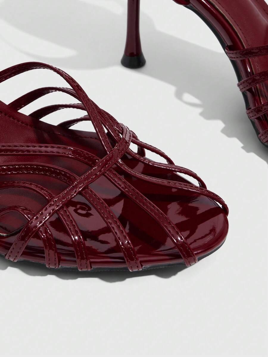 Women's glossy silver open-toed sandals with thin pyramid heel and strappy ribbon details.
