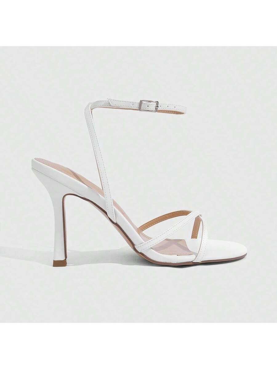 Pair of cream open-toe heeled sandals featuring crisscross front straps, a sleek stiletto high heel, and an adjustable ankle strap with buckle closure.