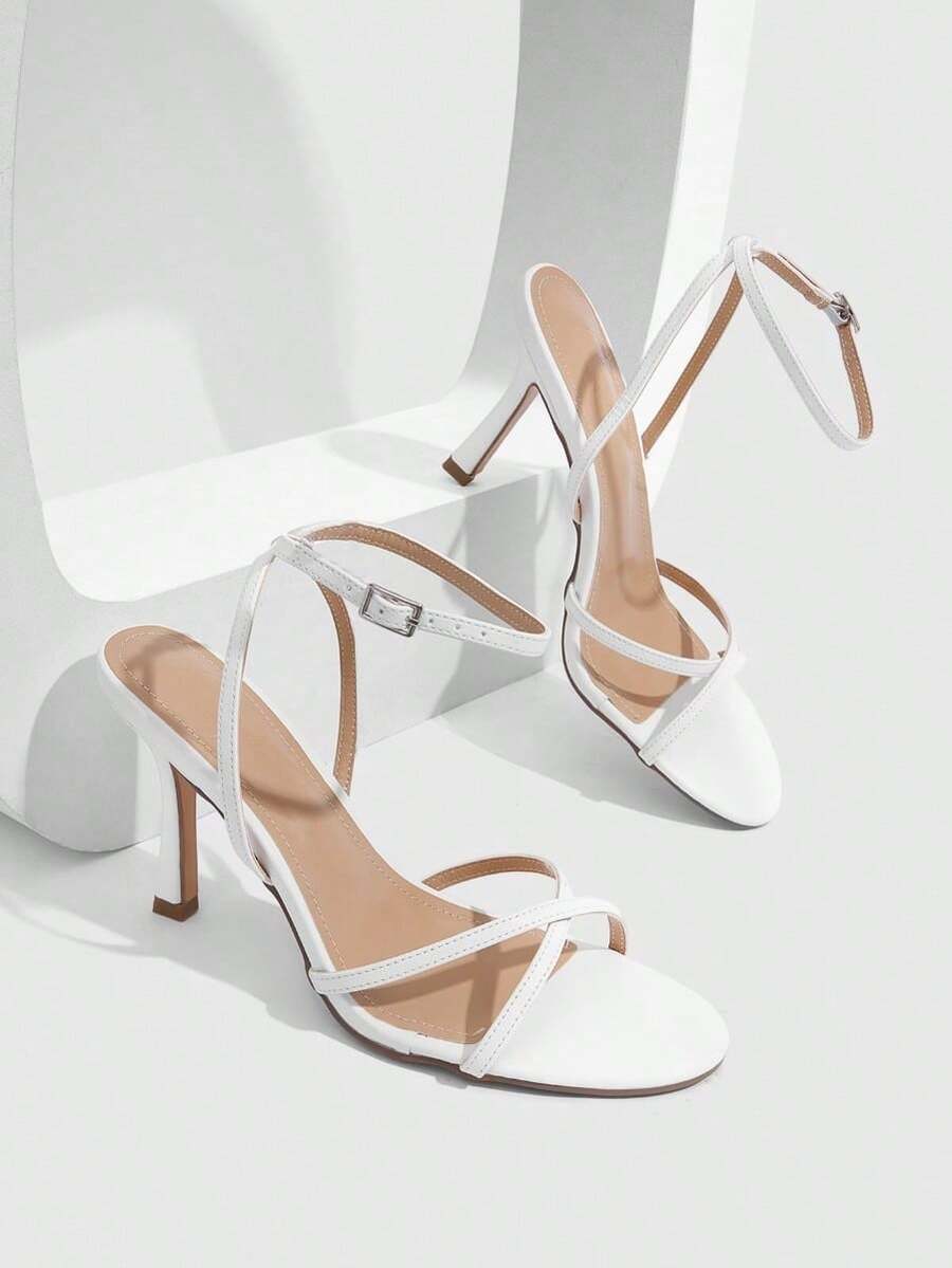 Pair of cream open-toe heeled sandals featuring crisscross front straps, a sleek stiletto high heel, and an adjustable ankle strap with buckle closure.