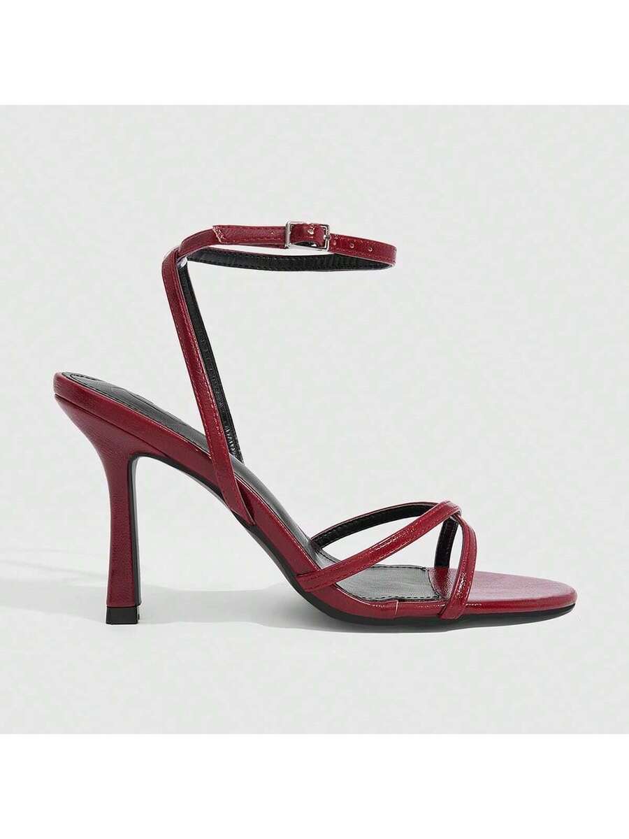 Pair of cream open-toe heeled sandals featuring crisscross front straps, a sleek stiletto high heel, and an adjustable ankle strap with buckle closure.