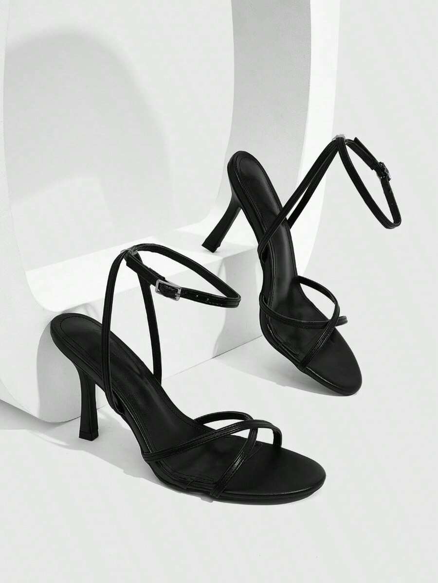Pair of cream open-toe heeled sandals featuring crisscross front straps, a sleek stiletto high heel, and an adjustable ankle strap with buckle closure.