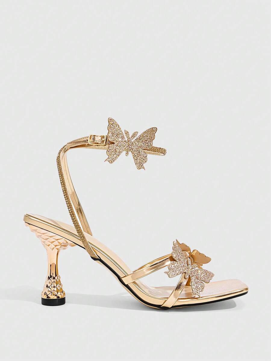 Glossy gold high heels featuring a sculptural heel, open-toe design, ankle strap buckle closure, and sparkling rhinestone butterfly embellishments.