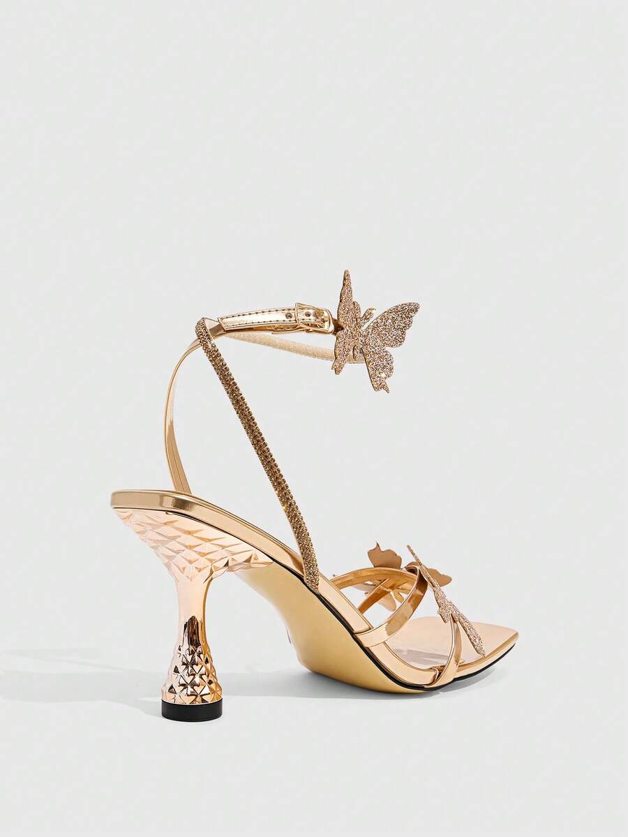 Glossy gold high heels featuring a sculptural heel, open-toe design, ankle strap buckle closure, and sparkling rhinestone butterfly embellishments.
