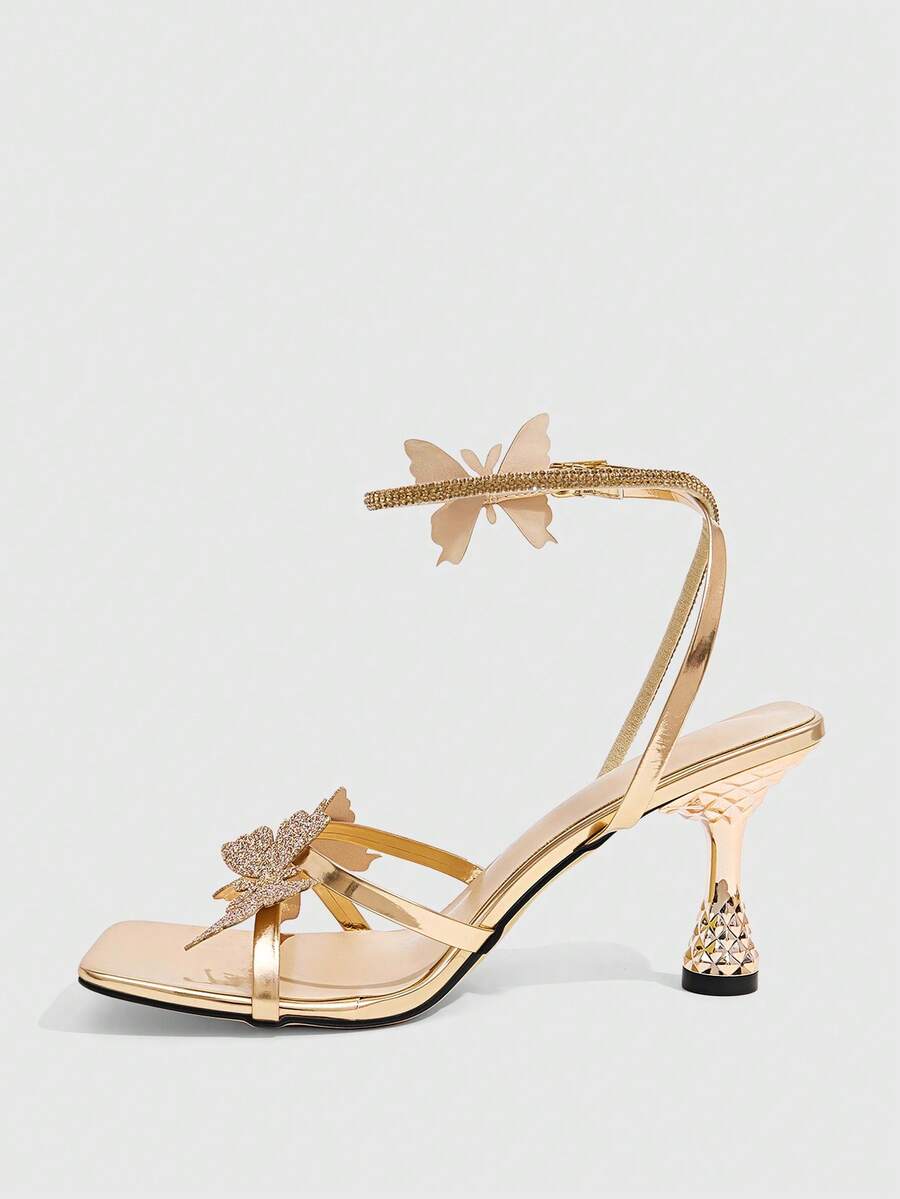 Glossy gold high heels featuring a sculptural heel, open-toe design, ankle strap buckle closure, and sparkling rhinestone butterfly embellishments.