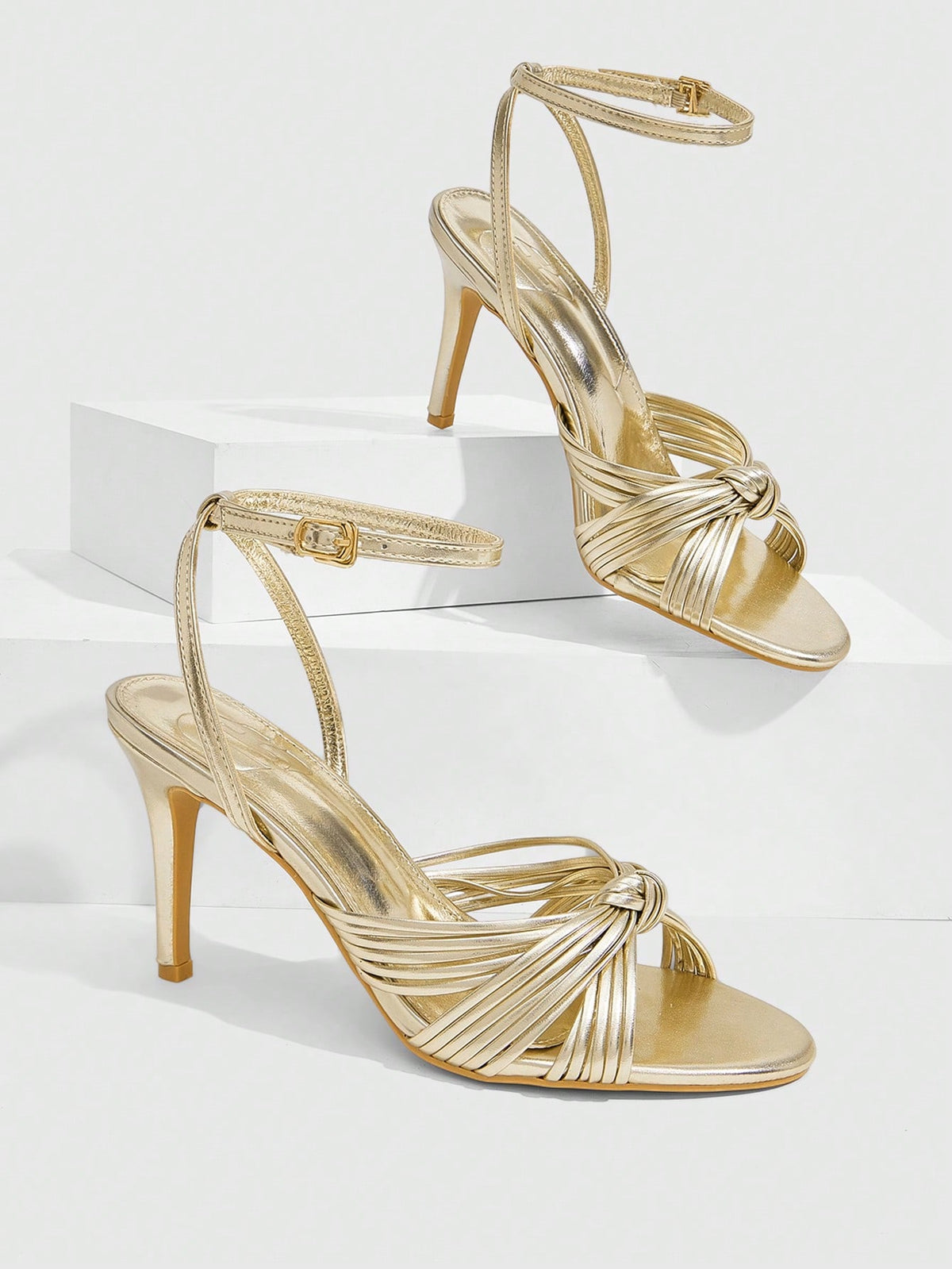 Women's champagne stiletto high heel sandals featuring knotted cross-over straps, open round toe, and adjustable ankle buckle strap.