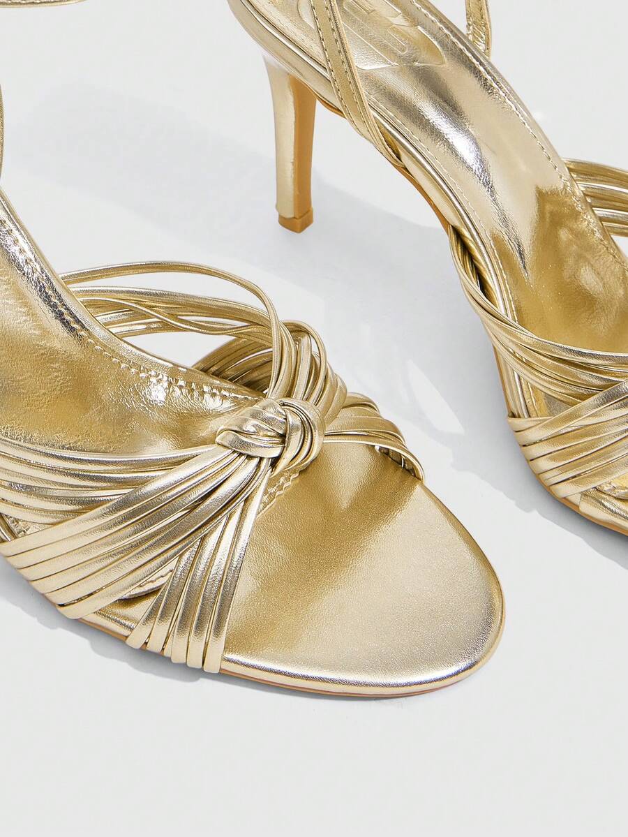 Women's champagne stiletto high heel sandals featuring knotted cross-over straps, open round toe, and adjustable ankle buckle strap.