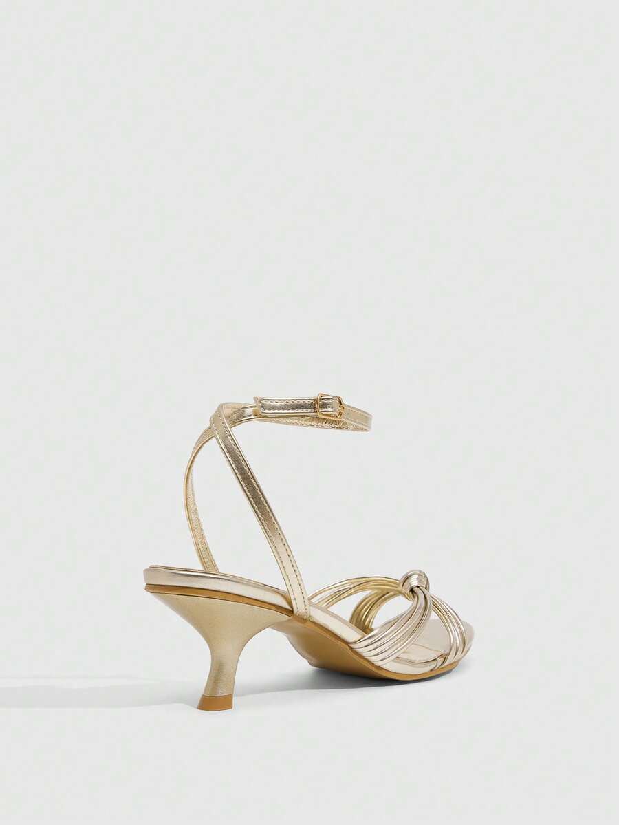 Women's champagne stiletto high heel sandals featuring knotted cross-over straps, open round toe, and adjustable ankle buckle strap.