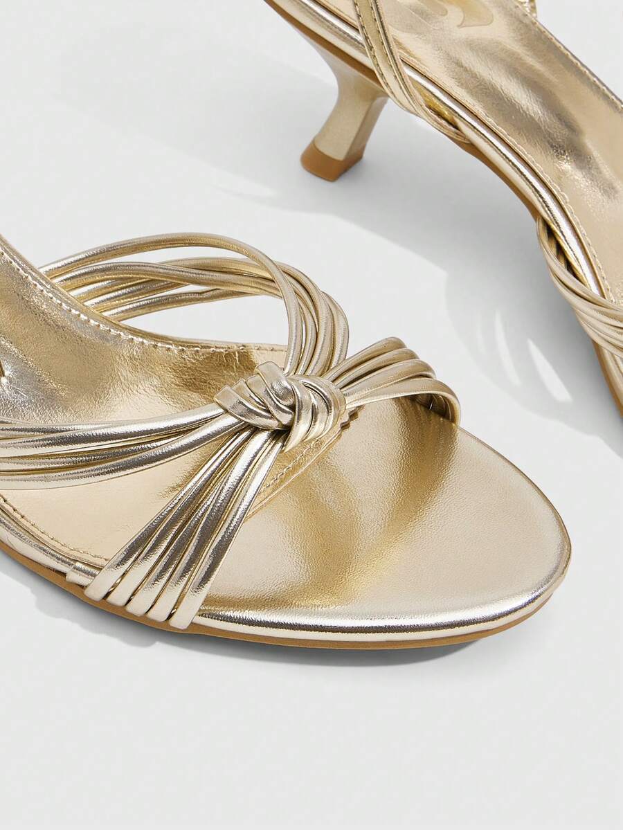 Women's champagne stiletto high heel sandals featuring knotted cross-over straps, open round toe, and adjustable ankle buckle strap.