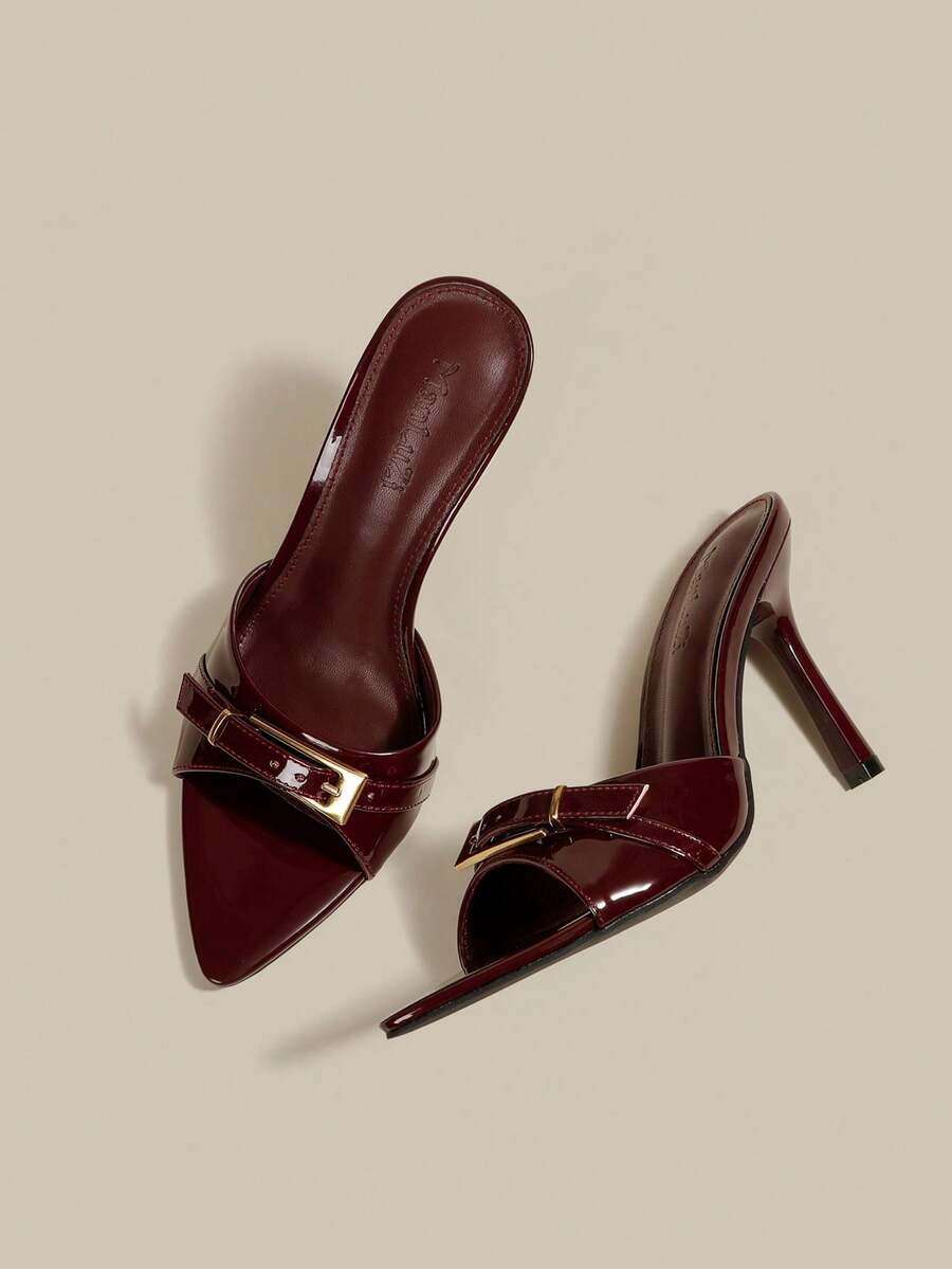 Black patent leather pointed toe mule sandals featuring stiletto high heels and decorative buckle detail for evening parties