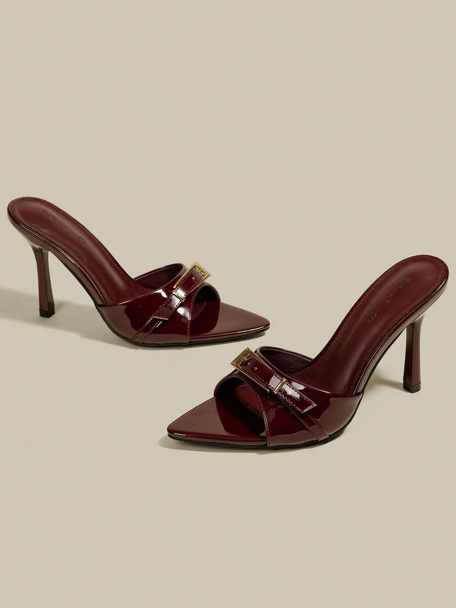 Black patent leather pointed toe mule sandals featuring stiletto high heels and decorative buckle detail for evening parties