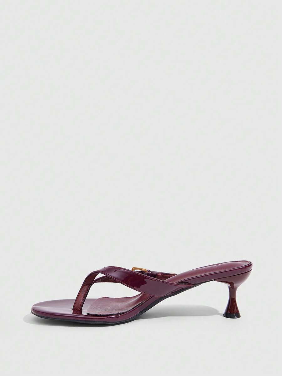 Women's patent leather heeled sandals featuring a toe post strap with metal buckle and mid pyramid heel.