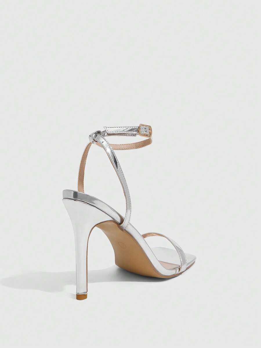Women's minimalist black heeled sandals featuring an open toe, stiletto high heel, and adjustable ankle strap buckle closure.