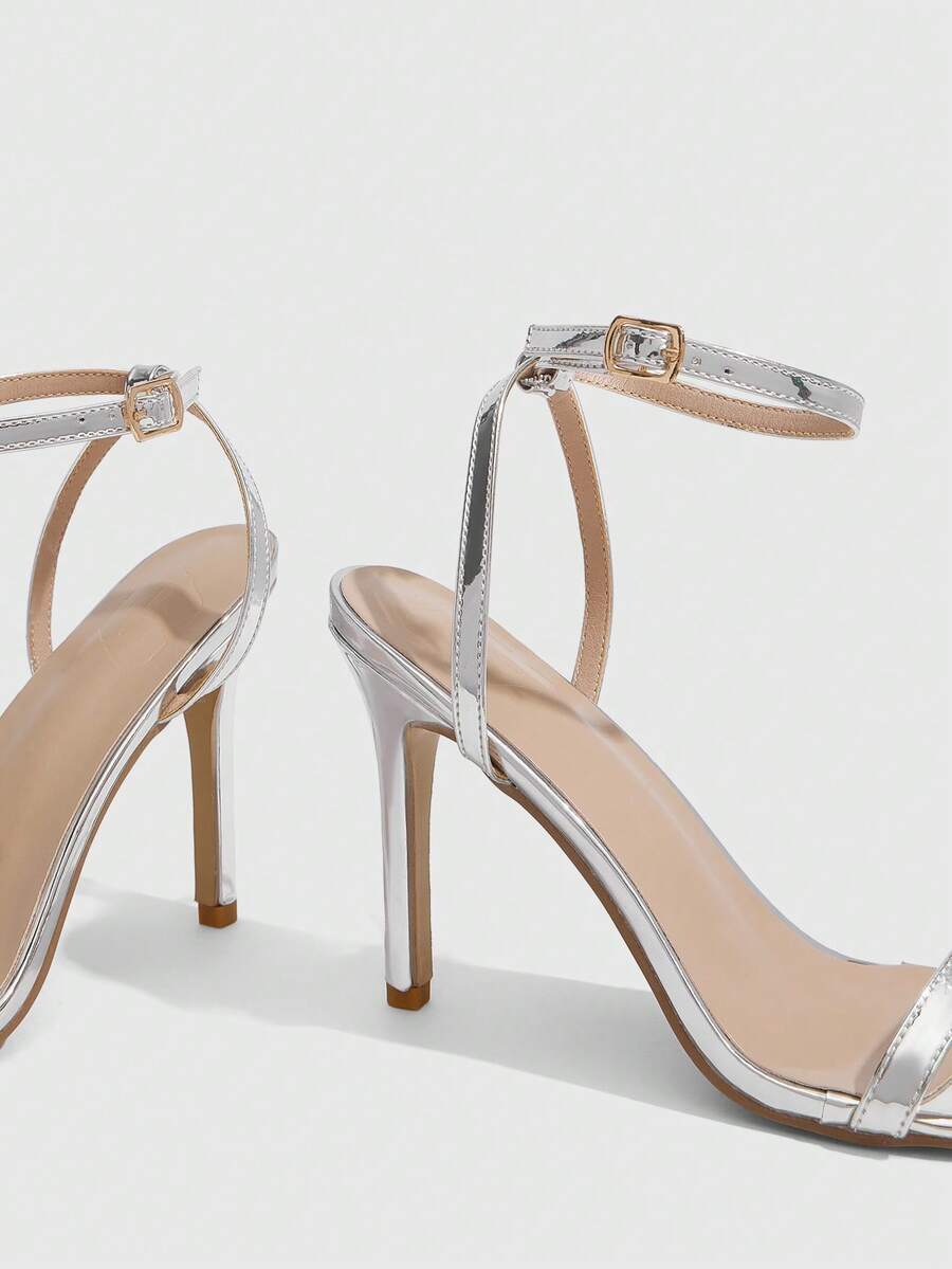 Women's minimalist black heeled sandals featuring an open toe, stiletto high heel, and adjustable ankle strap buckle closure.