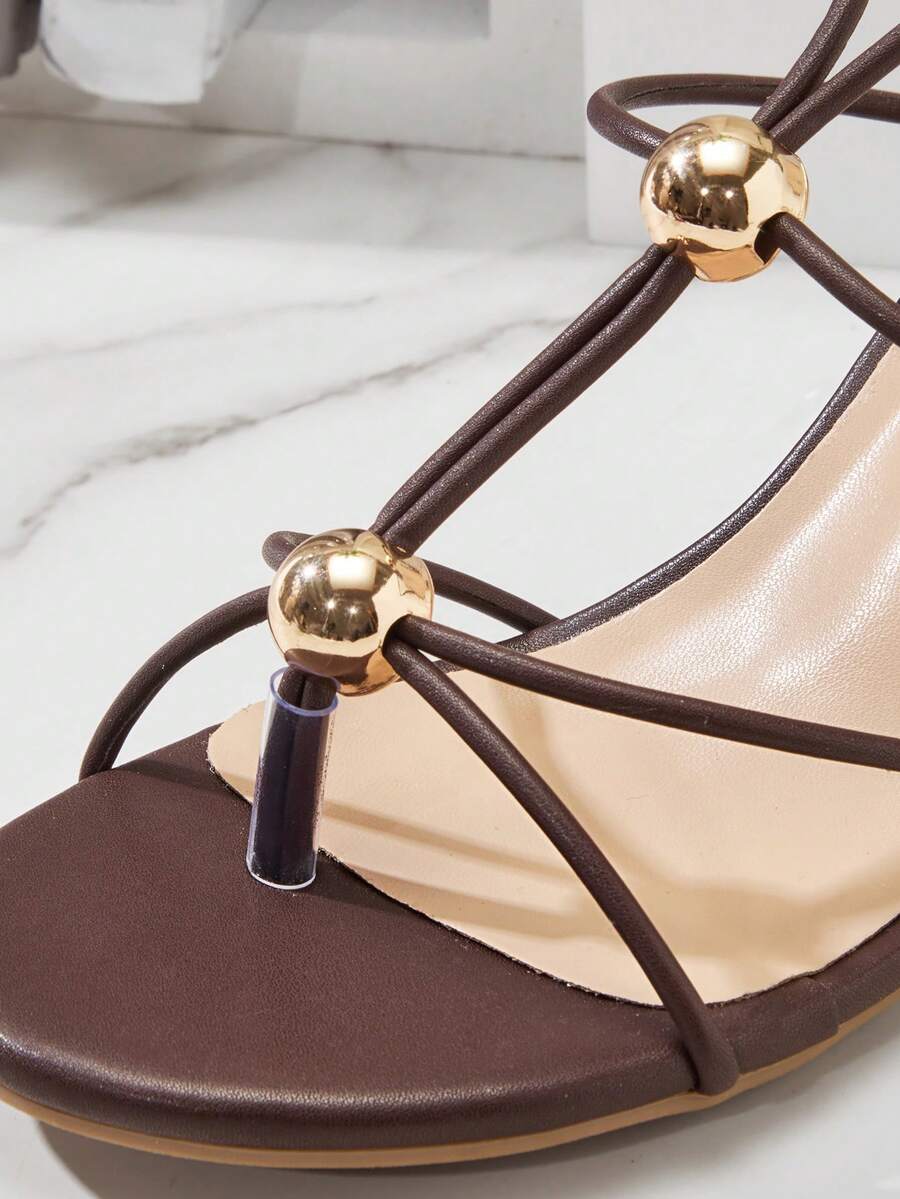 Women's strappy stiletto heel sandals crafted in vegan PU leather featuring open toe design and metallic bead accents.