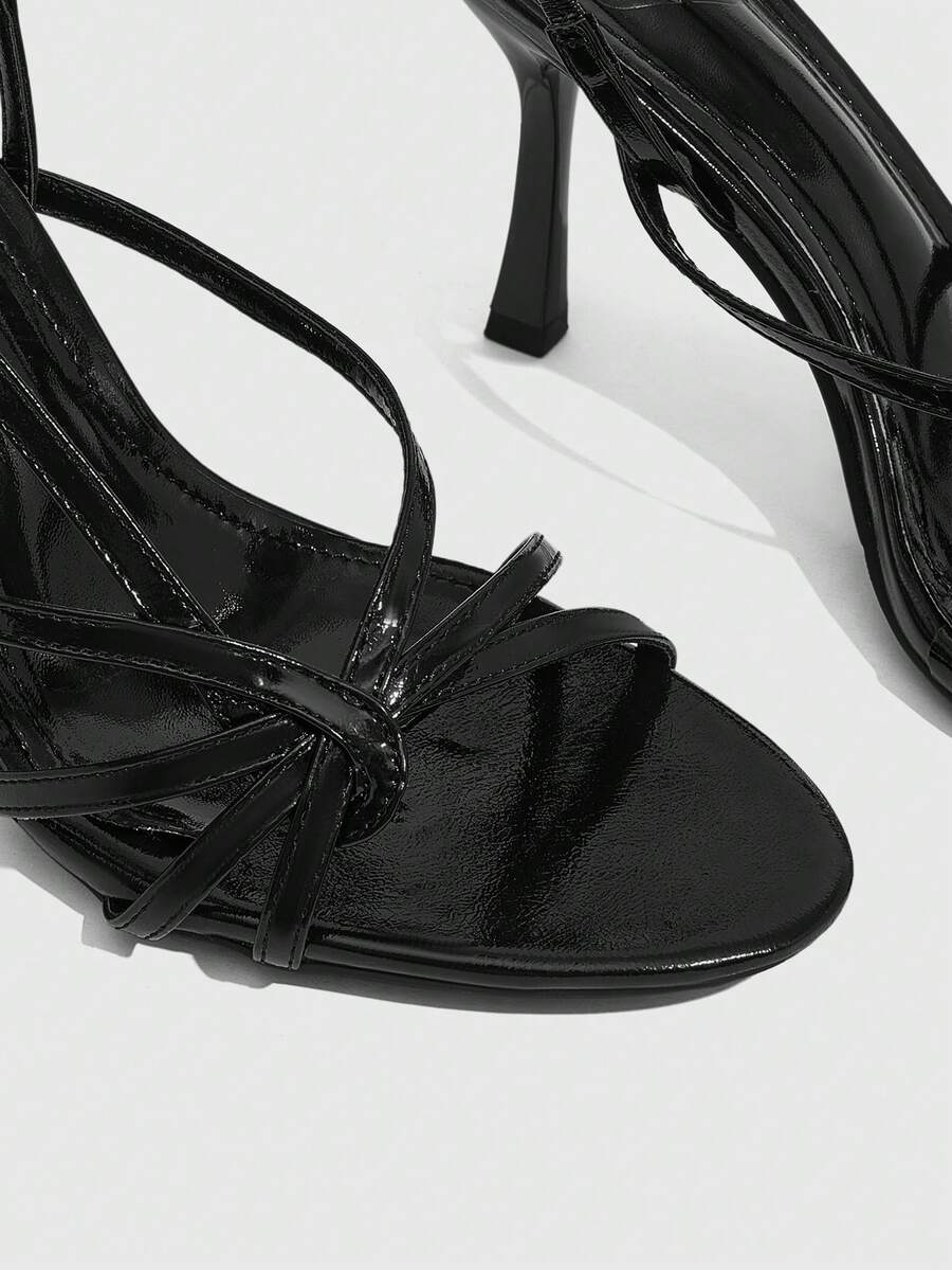 Women's open-toed stiletto high-heeled sandals in glossy patent black featuring twist strap detailing and slingback design.