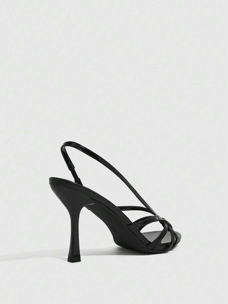 Women's open-toed stiletto high-heeled sandals in glossy patent black featuring twist strap detailing and slingback design.