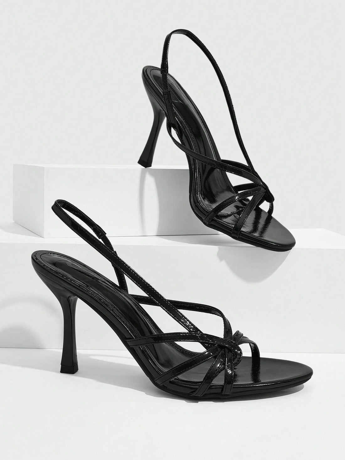 Women's open-toed stiletto high-heeled sandals in glossy patent black featuring twist strap detailing and slingback design.