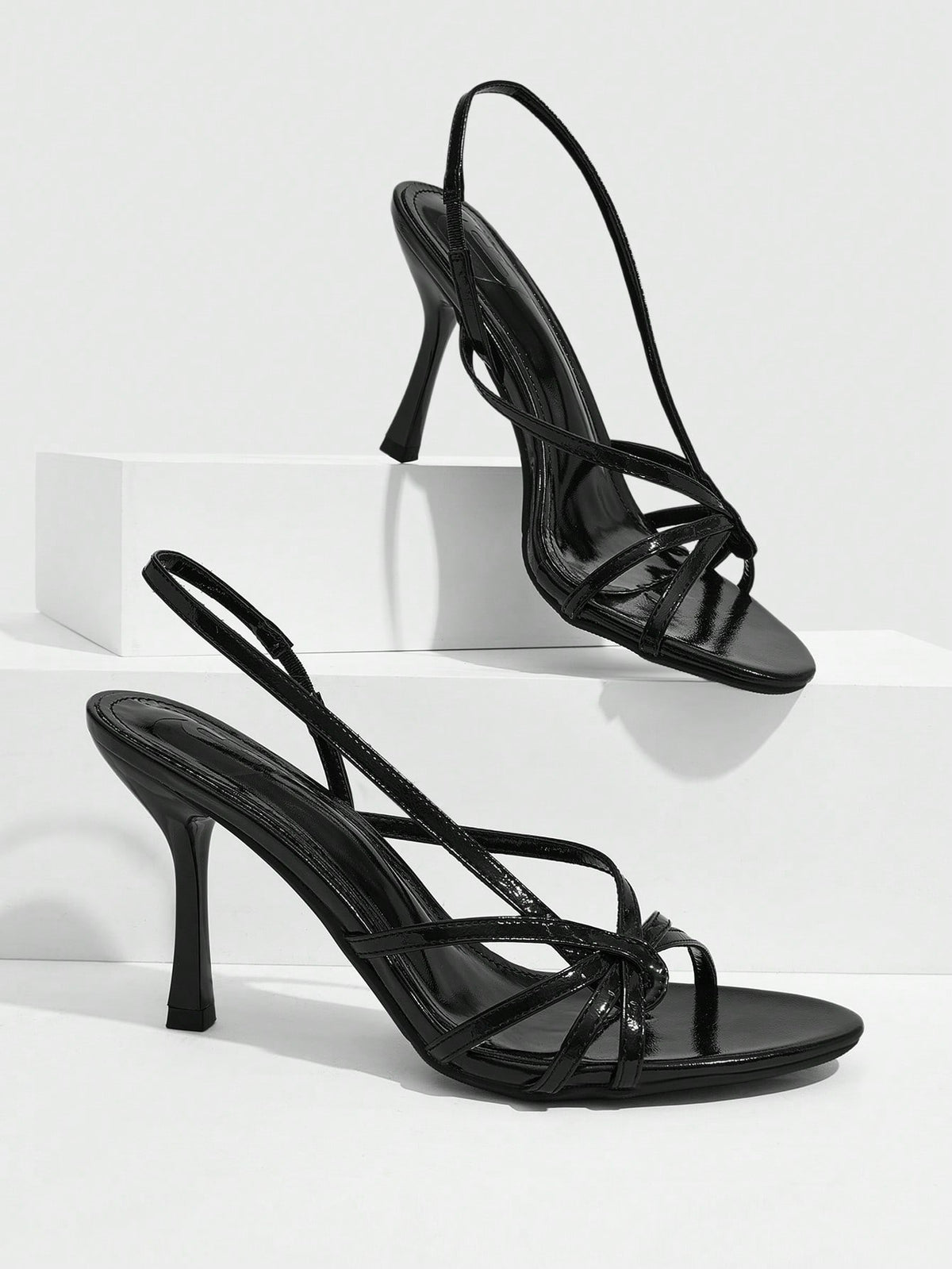 Women's open-toed stiletto high-heeled sandals in glossy patent black featuring twist strap detailing and slingback design.